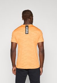 Orange camo-mønster T-shirt lavet af letvægtigt stof. Har rund hals og et sort mærke på ryggen, der siger "BORG".