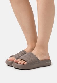 Des sandales d'été grises en caoutchouc présentent de larges bandages avec des détails texturés et un design ouvert à l'avant. La semelle est légèrement contournée.