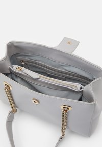 Grå strukturert håndveske laget av teksturert materiale, med gullhardware, en glidelåslomme og en glatt innerfôr. Dobbelt kjede detaljer.
