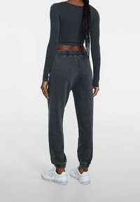 Donkergrijs geribbeld langemouw crop top, gecombineerd met bijpassende joggers, voorzien van een elastische tailleband en cuffs om de enkels, gedragen met witte sneakers.