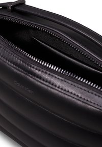 Czarny skórzany worek o fakturowanym wykończeniu. Posiada zamek błyskawiczny, wewnętrzną kieszeń oraz wytłoczone logo Calvin Klein z boku.