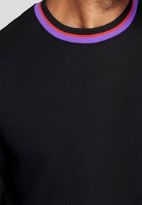 Schwarzes T-Shirt mit rundem Kragen und roten sowie lila Streifen, glatte Textur und kurzen Ärmeln. Nahaufnahme des Stoffs und des Halsausschnitts.