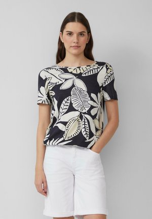 Marineblauw shirt met korte mouwen en een groot crèmekleurig loofpatroon, ronde halslijn, zachte textuur, gecombineerd met witte shorts. Minimalistisch ontwerp.