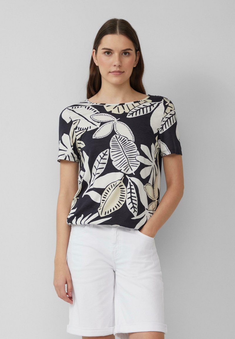 Chemise marine à manches courtes avec un grand motif de feuilles crème, col rond, texture douce, associée à un short blanc. Design minimaliste.