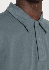 Light blue polo shirt with a soft texture, featuring a pointed collar, two snap buttons, and a clean, minimal design.