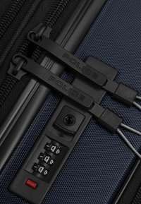 Primo piano di una valigia blu con doppia cerniera nera etichettata "POLICE", chiusa con un lucchetto TSA a combinazione nero.