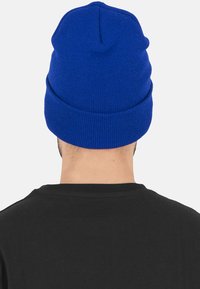 Caciula tricotată albastră cu mansetă împăturită, având un design texturat cu dungi. Stilul este simplu, potrivit pentru îmbrăcăminte casuală.