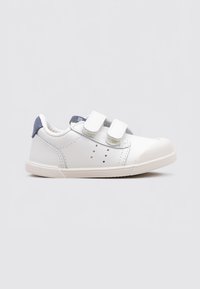 Zapatilla blanca de cuero con acento de tela azul en el talón, dos cintas de Velcro, punta redondeada y suela de goma. Detalles perforados en el costado.