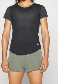 Svart tränings-t-shirt med ett strukturerat mönster, korta ärmar och en rundad fåll, kombinerad med ljusgröna shorts.