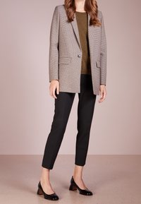 Blazer à carreaux beige et marron, associé à un top vert olive, un pantalon noir sur mesure, et des chaussures à talons blocs noirs brillants.