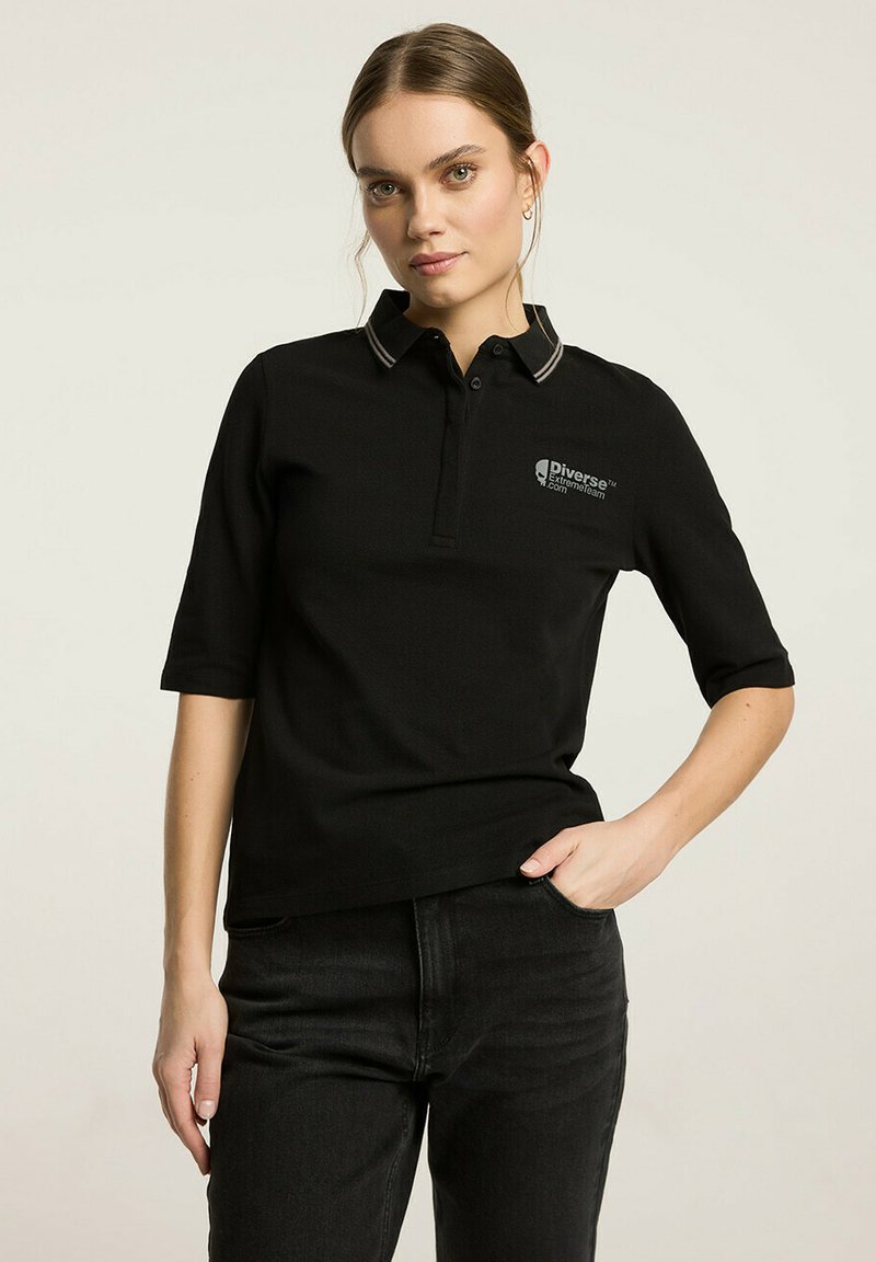 Czarna koszulka polo wykonana z bawełny, z krótkimi rękawami, kołnierzykiem z szarymi paskami i logiem na lewej piersi. Stylizowana z ciemnymi dżinsami.