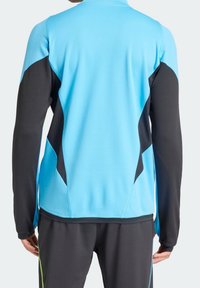 Långärmad atletisk topp med en klarblå kropp, svarta ärmar och texturerade sidopaneler. Tillverkad av lätt, fuktavledande tyg.