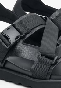 Zwarte sandalen met een textuur leer bovenwerk en verstelbare nylon banden, uitgerust met een stevige kunststof gesp en een gevoerde zool.