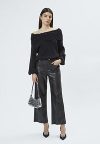 Schwarzer, schulterfreier Pullover mit strukturiertem Ripp-Ausschnitt, kombiniert mit weiten, faux-ledernen Hosen, schwarzen spitzen Schuhen und einer silbernen Tasche.