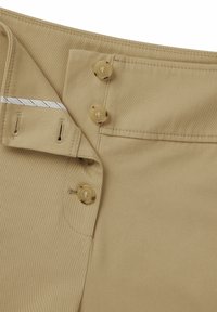 Beiga byxor med en slät textur, med två stora knappar och låsning. Inkluderar detaljer med stikningar på fickorna.