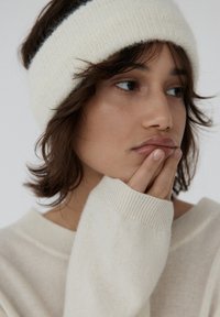 Bia�ła dzianinowa opaska na głowę z czarnym paskiem, zestawiona z jasnym, teksturowanym swetrem z prążkowanymi mankietami.