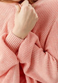 Różowy sweter z dzianiny o teksturowanym wzorze i prążkowanymi mankietami, z luźnymi rękawami i swobodnym krojem, prezentujący miękki, przytulny wygląd.