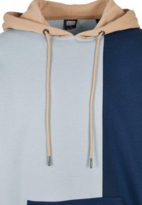 Sweat à capuche avec capuche beige, cordons de serrage beiges et un design fendu à l'avant en bleu clair et bleu marine.