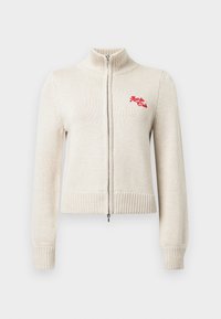 Pull zippé beige avec col et poignets côtelés. Présente un petit logo rouge "Après Club" sur la poitrine gauche. Texture tricot douce.