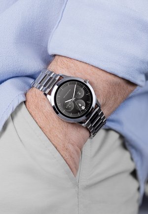 Silberner Metallarmbanduhr mit einem schwarzen Zifferblatt, drei kleinen Ziffernblättern und einer Datumsanzeige, die mit einem Armband aus Edelstahl gesichert ist.
