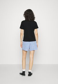 Svart kortärmad skjorta i kombination med blå mönstrade shorts med små vita blommor. Modellen bär svarta hög-top sneakers med vita sulor.