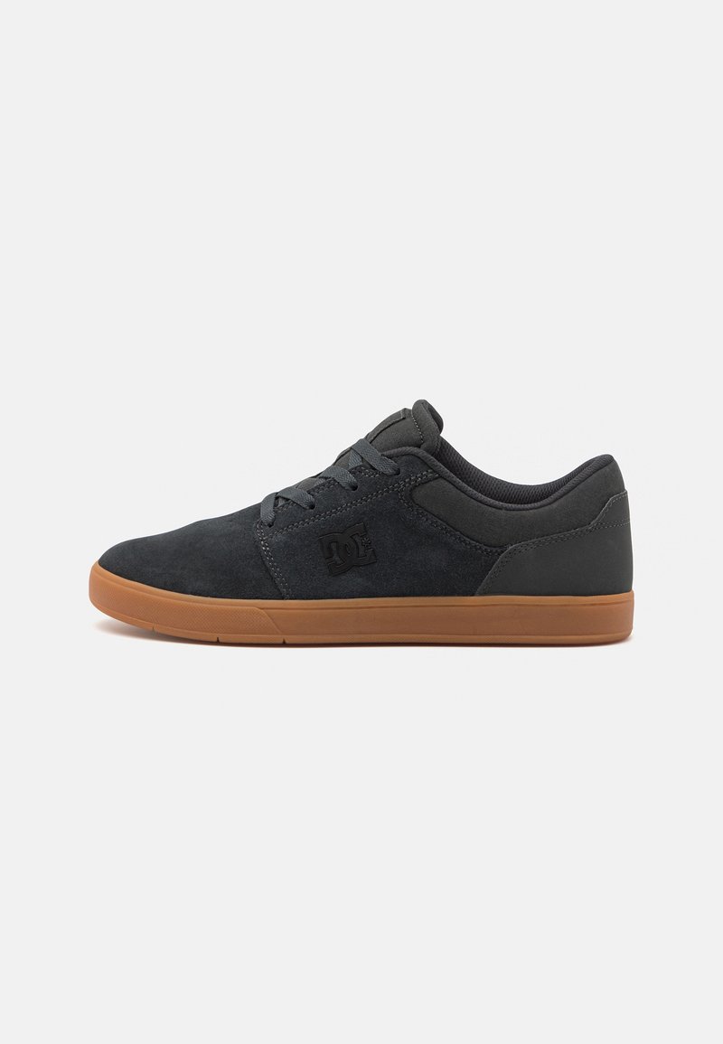 Dark grey suede sneakers with a rubber tan sole, featuring a black logo on the side and textured accents on the upper.