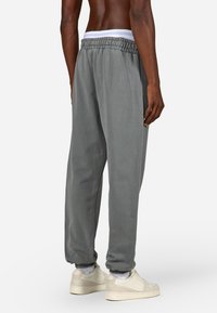 Pilkos sportinės kelnės su elastinga juosmeniu ir rankovėmis, pasižyminčios švelniu tekstūru ir laisvu siluetu. Dėvimos su šviesios spalvos sportbačiais.