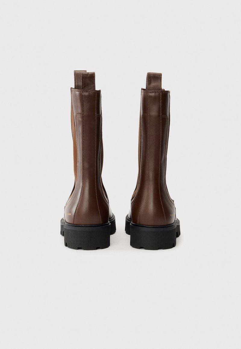 Ein Paar braune Leder-Stiefeletten mit schwarzen klobigen Sohlen, Hinterziehschlaufen und dezenten Nähdetails, von hinten auf weißem Hintergrund gezeigt.