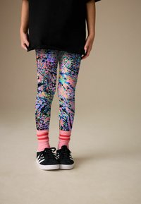 Colanți colorați și cu modele în roz, albastru și negru, purtați cu șosete roz cu dungi și adidași negri cu accente albe.