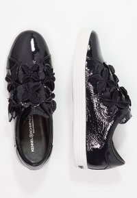 Baskets en cuir verni noir avec des accents floraux noirs décoratifs, semelle en caoutchouc blanc, bout arrondi et surface texturée.
