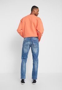 Oransje genser med avslappet passform, sammen med lyseblå denimjeans. Joggesko med hvit såle og svart stoff fullfører antrekket.