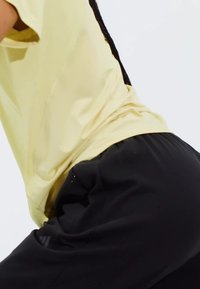 Helles gelbes Sportshirt, kombiniert mit schwarzen Sporthosen. Das Outfit bietet eine entspannte Passform und einen glatten Stoff. 