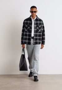 Svart og hvit rutete overskjorte, hvit skjorte under, grå jeans, og svarte støvler. Tilbehør: svart totebag, mørke solbriller.