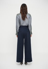 Chemise à rayures bleues à manches longues avec une touche de vert, associée à un pantalon large marine avec deux poches arrière et un ourlet retroussé.