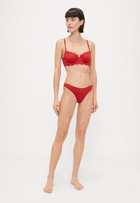 Sutien roșu din dantelă, cu sârmă de susținere și bretele ajustabile, asociat cu un thong roșu fără cusături asortat. Textură netedă, model floral pe sutien.