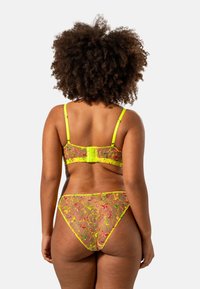 Genomskinligt mesh-lingerie-set med livfull blommönstring i rosa och grönt, med neongula detaljer och justerbara band.
