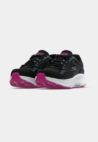 Chaussures de sport noires avec accents roses, dotées d'une tige texturée, d'une semelle intermédiaire blanche amortissante et d'une semelle extérieure en caoutchouc à motifs pour une meilleure adhérence.