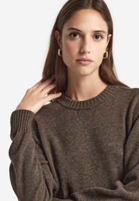 Pull en tricot marron avec un col rond et des poignets côtelés. Le tissu a une texture douce, avec un motif chiné subtil.