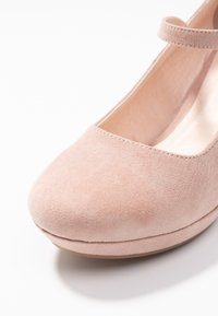 Scarpa Mary Jane in suede rosa con punta arrotondata e una cinturino sul dorso del piede. La suola è leggermente rialzata, con un rivestimento interno liscio.