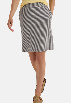 Femme portant une jupe grise et blanche rayée verticalement, longueur genou, un haut jaune et des sandales ouvertes beige avec des brides à boucle.