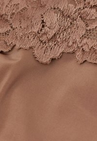 Underklädesmaterial med en mjuk, slät textur i en varm brun ton. Toppen har intrikata spetsdetaljer med en scalloped kant.