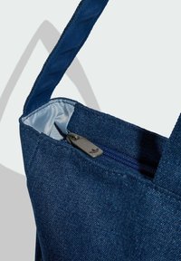 Borsa tote in denim di colore blu scuro, con cursore della cerniera argentato e fodera interna liscia. Include robuste cinghie per il trasporto.