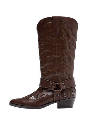 Brązowy skórzany kowbojski but z ozdobnym przeszyciem, paskiem z uprzęży i niskim, warstwowym obcasem, przedstawiony z profilu na białym tle.