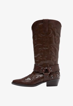 Brązowy skórzany kowbojski but z ozdobnym przeszyciem, paskiem z uprzęży i niskim, warstwowym obcasem, przedstawiony z profilu na białym tle.