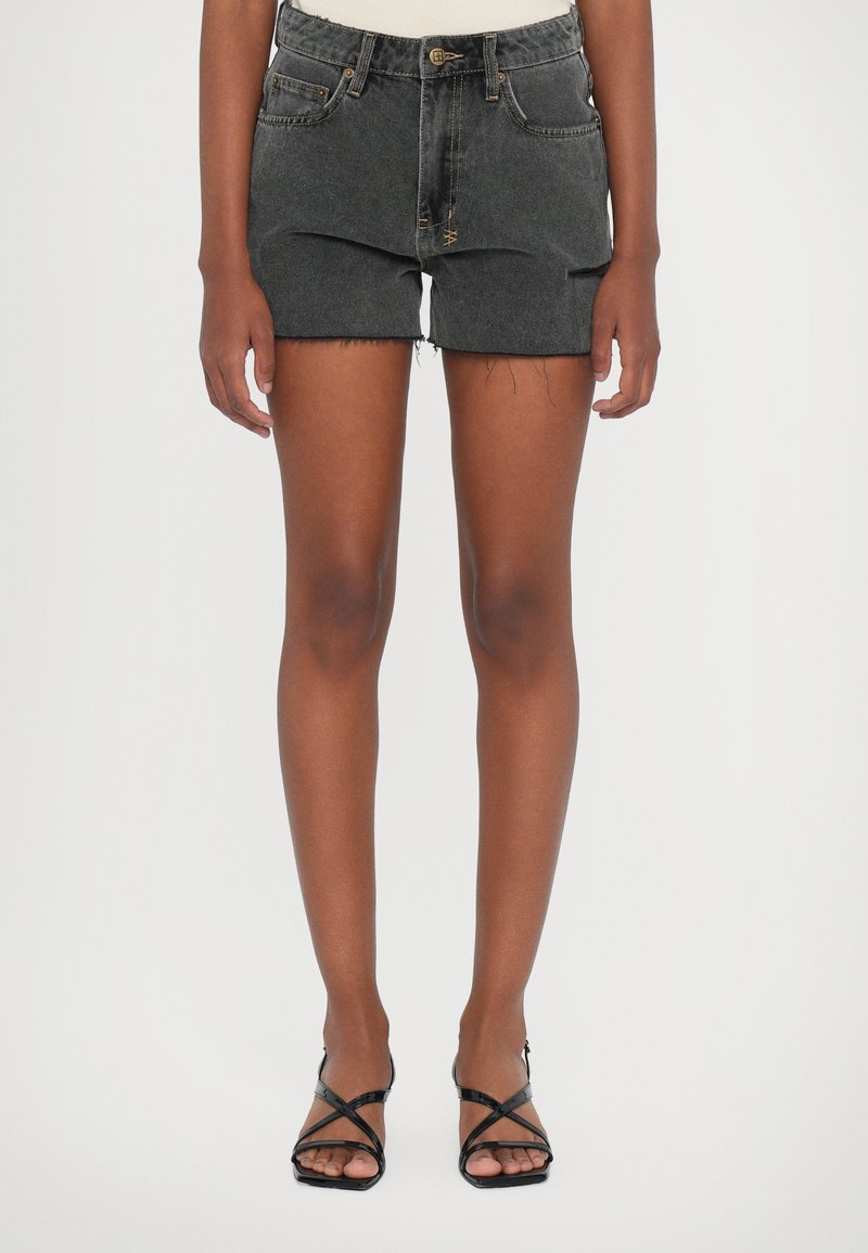Dark gray denim shorts with frayed hems, five pockets, and a button closure. Worn with black strappy sandals, showcasing legs and shoes.
