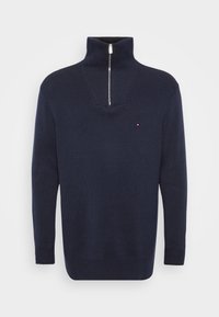 Granatowy sweter z ribbingu z wysokim kołnierzem i zapięciem na pół suwak. Posiada mały akcent logo na klatce piersiowej. Wykonany z teksturowanej tkaniny.