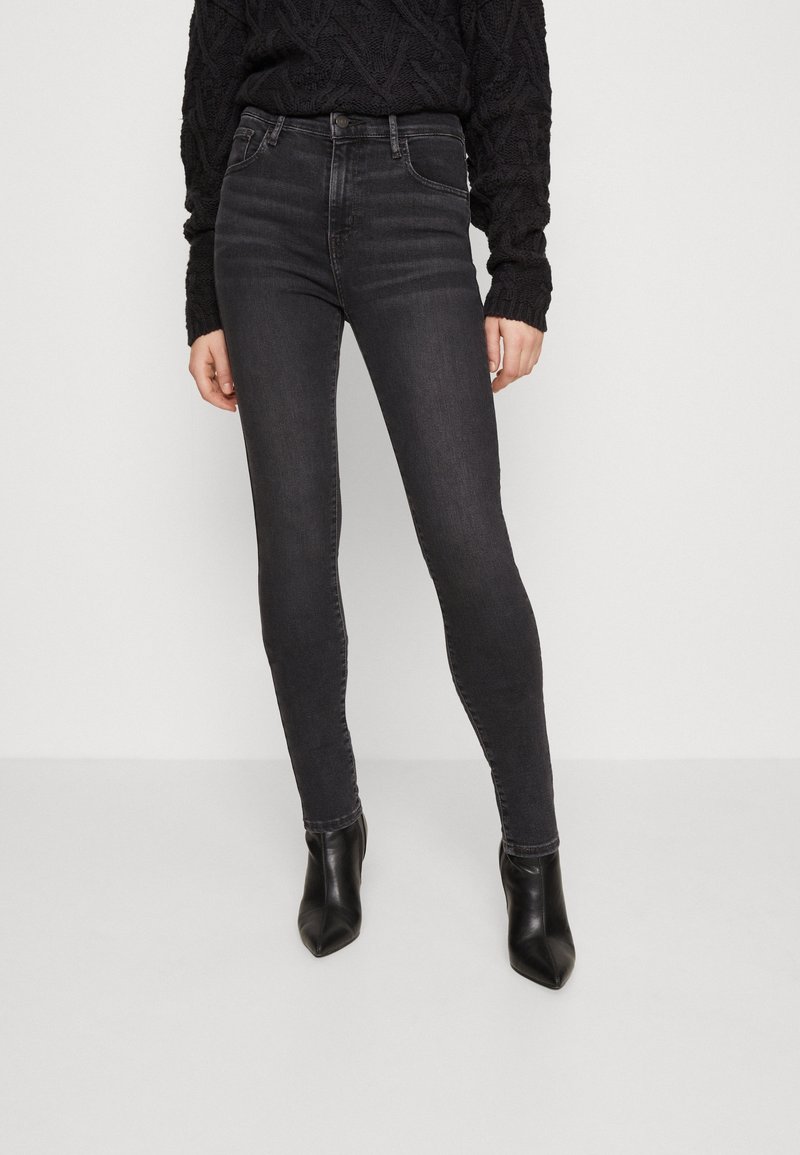 Jeans skinny negros de denim, con una textura suave, talle alto y un desvanecimiento mínimo. Combinados con botines negros de tacón puntiagudos.