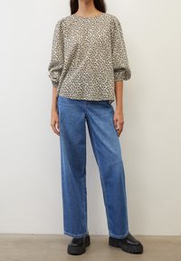 Blusa larga con motivo floreale in beige e verde scuro, abbinata a jeans a gamba larga blu e stivali platform neri spessi.
