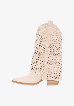 Beige suède cowboylaars tot halverwege de kuit met geometrische laseruitgesneden patronen, gestapelde houten hak en een lus aan de bovenkant.