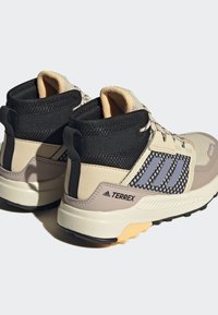 Zapatillas deportivas de media altura en beige y negro con acentos grises, paneles de malla, tejido texturizado y suelas de goma con patrones de agarre.